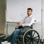 Man in a wheelchair sitting in front of a whiteboard with graphs and charts.